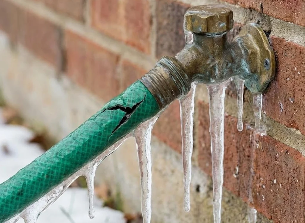 Frozen outdoor faucet with attached hose and ice damage — reminder of what happens without plumbing prep.